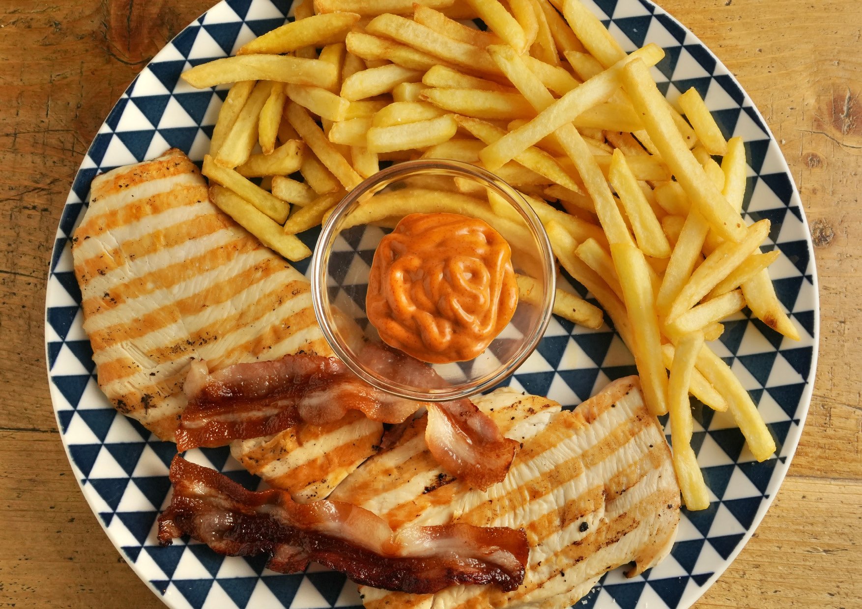 Petto di pollo ai ferri servito con pancetta alla piastra, patate stick e salsa della casa